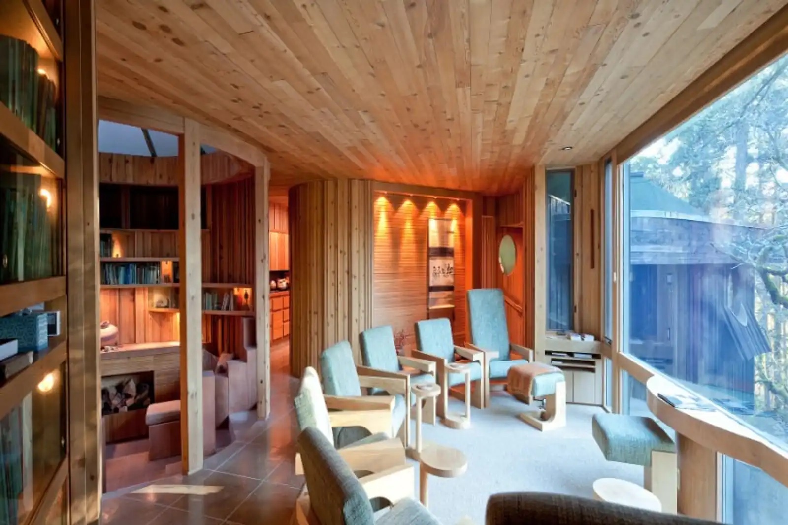Living room at Hunter House with cedar-slat ceiling, blue-green armchairs, and floor-to-ceiling windows facing the forest.